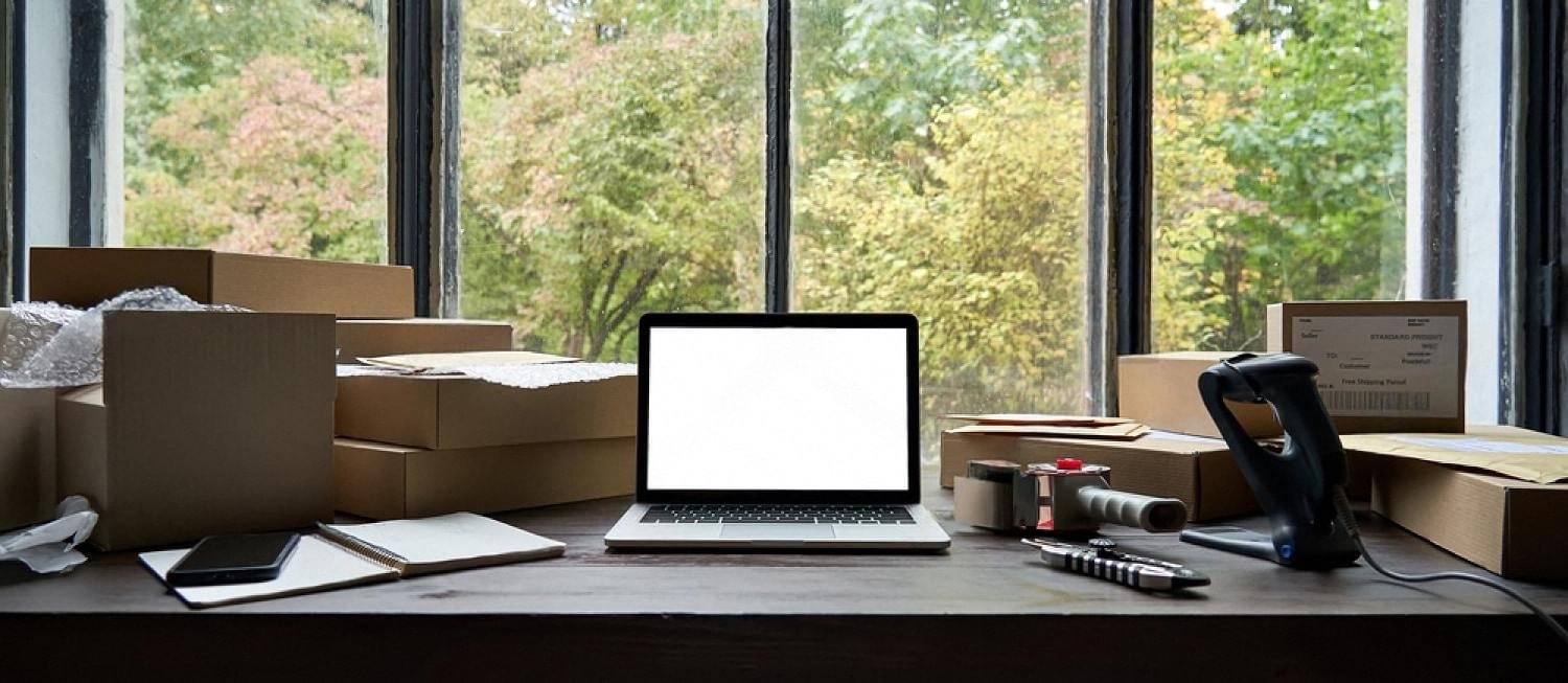 Home office desk with a laptop, packing boxes and a barcode scanner used to prepare rental equipment